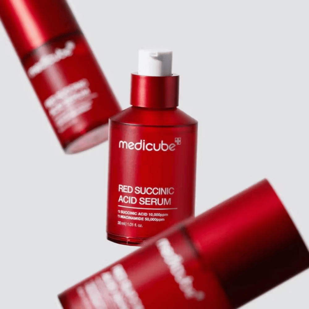Medicube Red Succinic Acid Serum in roter Pumpflasche, umgeben von mehreren identischen Flaschen vor hellem Hintergrund. Das Produkt enthält Bernsteinsäure und Niacinamid zur Behandlung von Akne und Pigmentflecken.