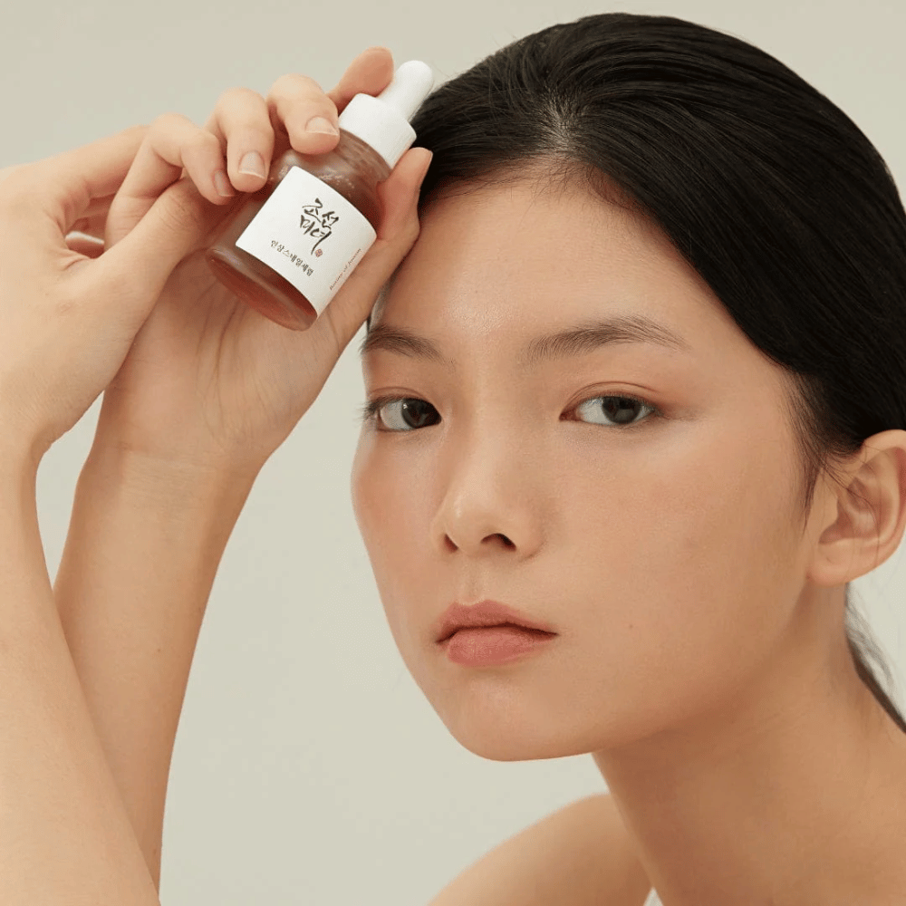 Modell hält Beauty of Joseon Revive Serum an der Wange – nährstoffreiches Serum mit Ginseng und snail mucin.
