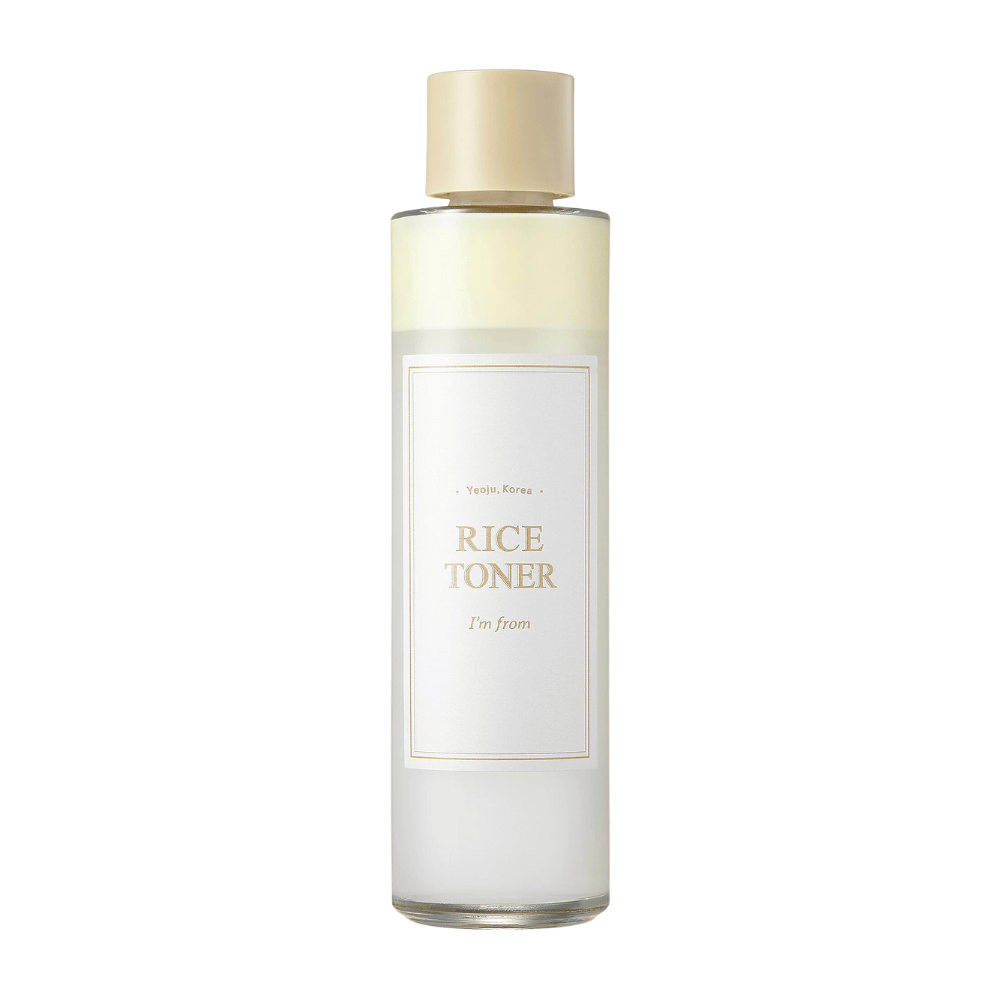 Eine transparente Flasche mit goldenem Deckel und einem Etikett, das "Rice Toner I'm from Yeojü, Korea" angibt. Die Flasche enthält eine helle Flüssigkeit, wahrscheinlich ein Toner auf Reisbasis. Das Design ist sauber und minimalistisch. Der Hintergrund ist weiß.