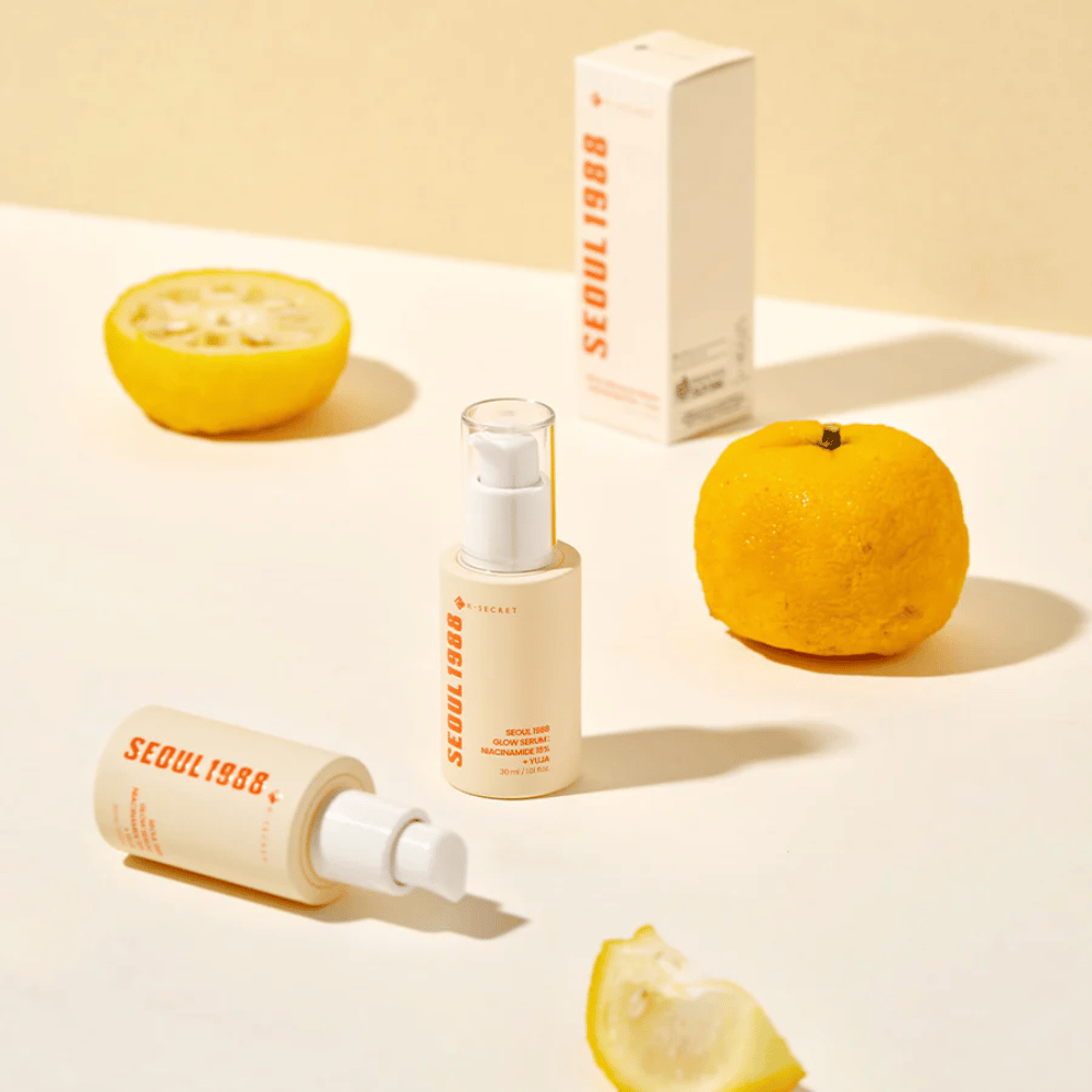 Mehrere Flaschen und Verpackungen von Seoul 1988 Glow Serum arrangiert mit ganzen und halbierten Yujafrüchten im Hintergrund.