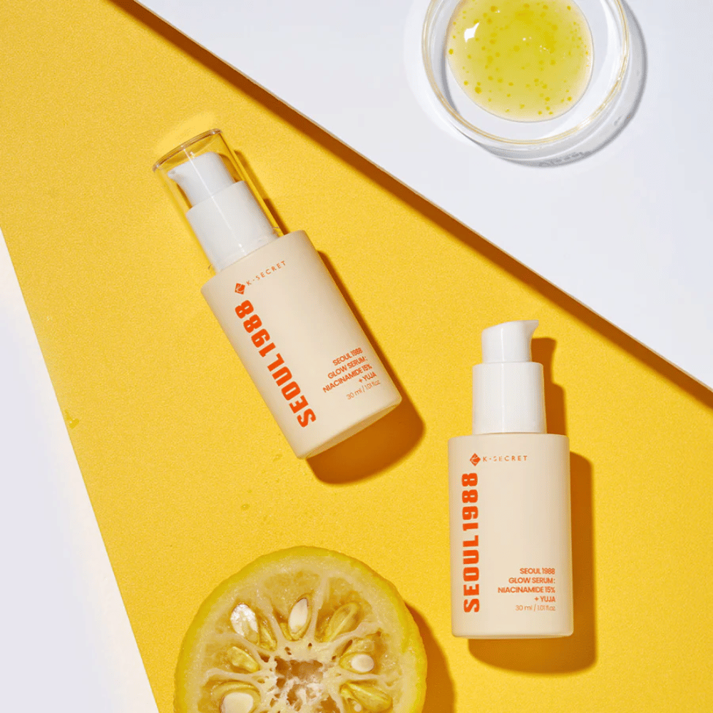 Zwei Flaschen Seoul 1988 Glow Serum auf gelbem Hintergrund zusammen mit einer Schale mit gelbem Serum und einer halbierten Zitrusfrucht platziert.