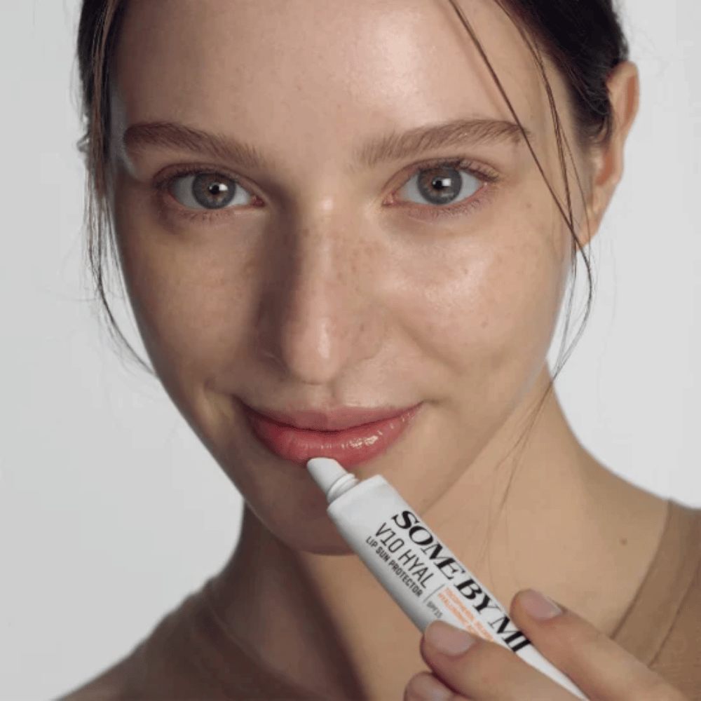 Eine Frau hält eine Tube V10 Hyal Lip Sun Protector SPF15 7ml Lippenbalsam für Sonnenschutz und Feuchtigkeitspflege, von SOME BY MI.