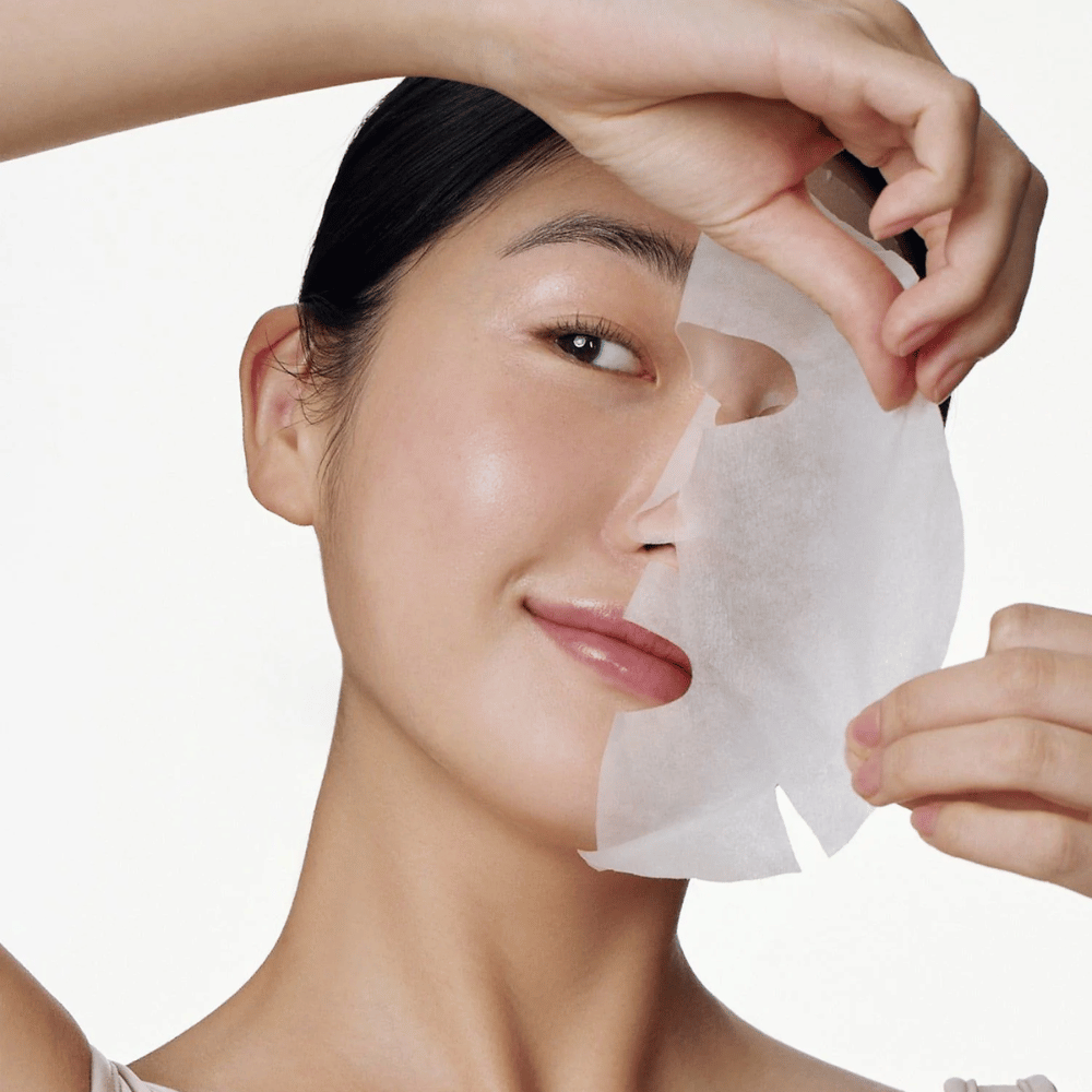 Dieses Bild zeigt eine Person, die eine Gesichtsmaske verwendet, speziell "Galactomyces Glutathione Daily Mask" von Some By Mi. Die Maske hellt die Haut auf und verleiht ihr einen strahlenden Glanz, während sie die Haut dank Inhaltsstoffen wie Glutathion und Vitamin C tiefgehend pflegt und mit Feuchtigkeit versorgt.