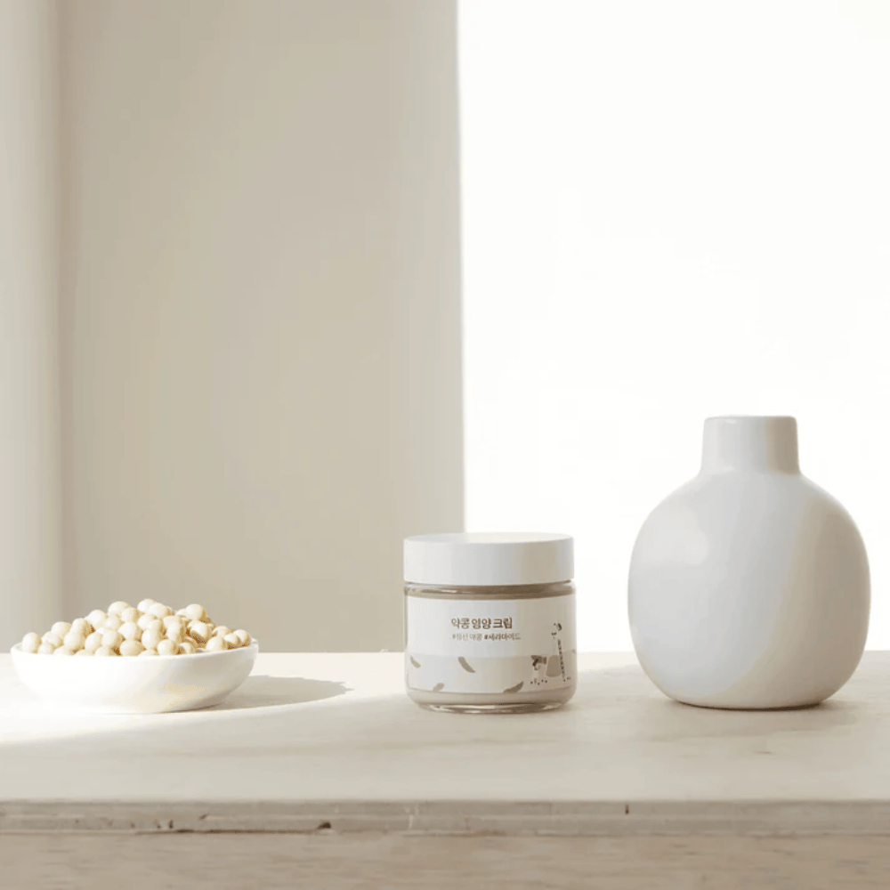 Mixsoon Soybean Nourishing Cream steht auf einem Holztisch neben einer Vase und Sojabohnen. Eine minimalistische, feuchtigkeitsspendende Creme mit natürlichen Zutaten.