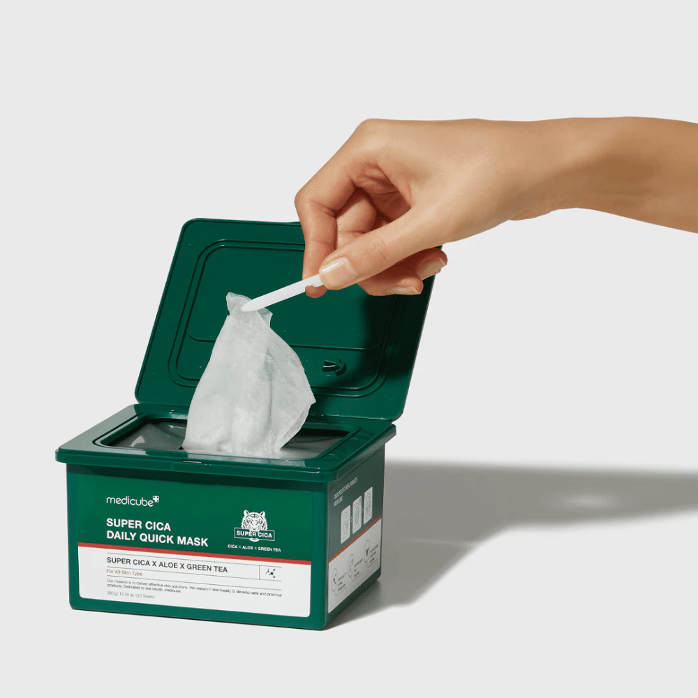 Grüner Behälter mit offenem Deckel zeigt medicube Super Cica Daily Quick Mask. Eine Hand zieht eine Tuchmaske mit der mitgelieferten Pinzette heraus. Das Produkt enthält Cica, Aloe und grünen Tee, ideal für schnelle Feuchtigkeitspflege und beruhigende Wirkung.