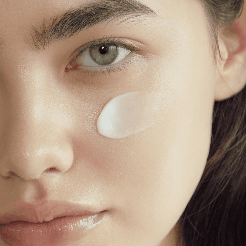 Nahaufnahme der Haut mit auf die Wange aufgetragener Creme, um das feuchtigkeitsspendende, weichmachende und strahlende Finish auf der Haut zu zeigen.