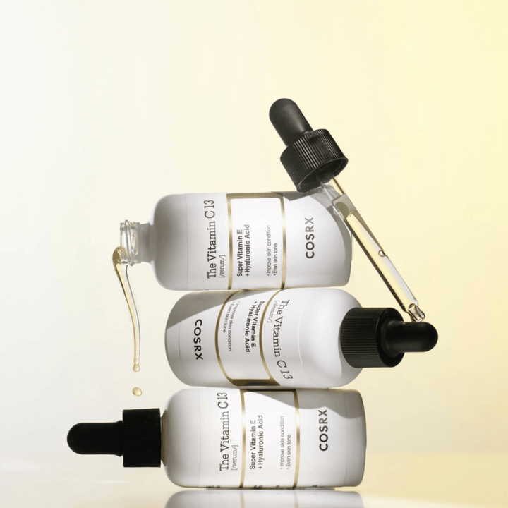 COSRX The Vitamin C 13 Serum mit Vitamin E und Hyaluronsäure, drei Flaschen mit Pipette und Tropfen von Vitamin-C-Serum gegen ungleichmäßigen Hautton und Strahlkraft.