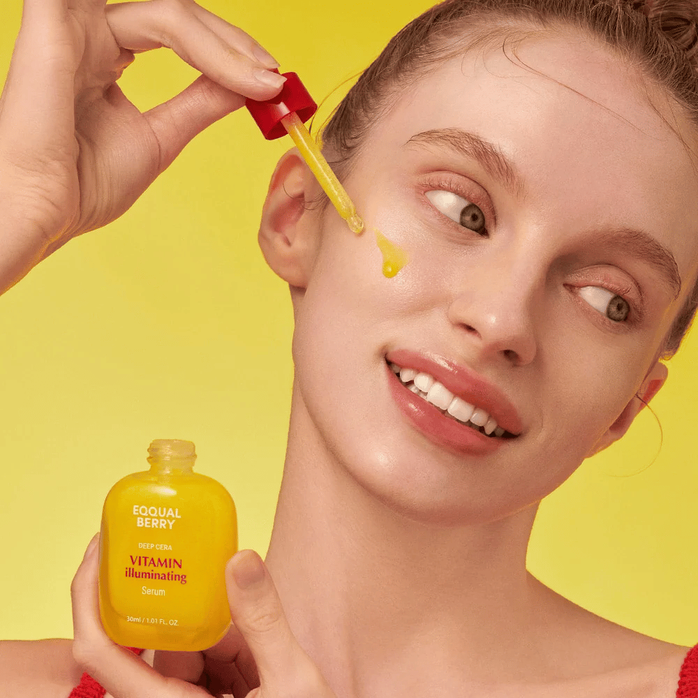 Lächelnde Frau trägt Equal Berry Vitamin Illuminating Serum mit einer Pipette auf. Frische und strahlende Haut vor einem lebhaften gelben Hintergrund, der zur Farbe des Serums passt.
