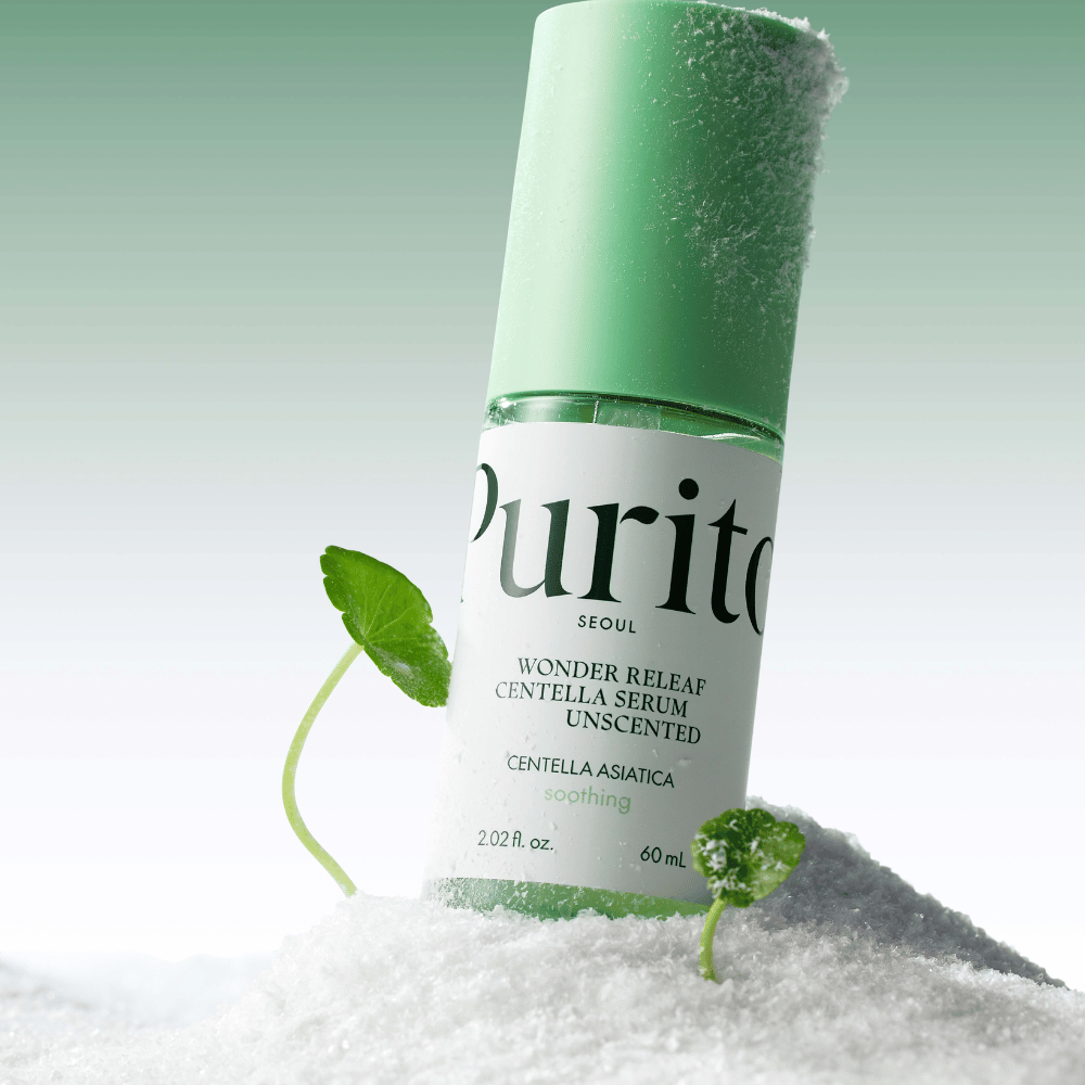 Flasche mit Purito Centella Serum liegt im Schnee, grüne Blätter sind sichtbar, vor einem weichen grünen Hintergrund.
