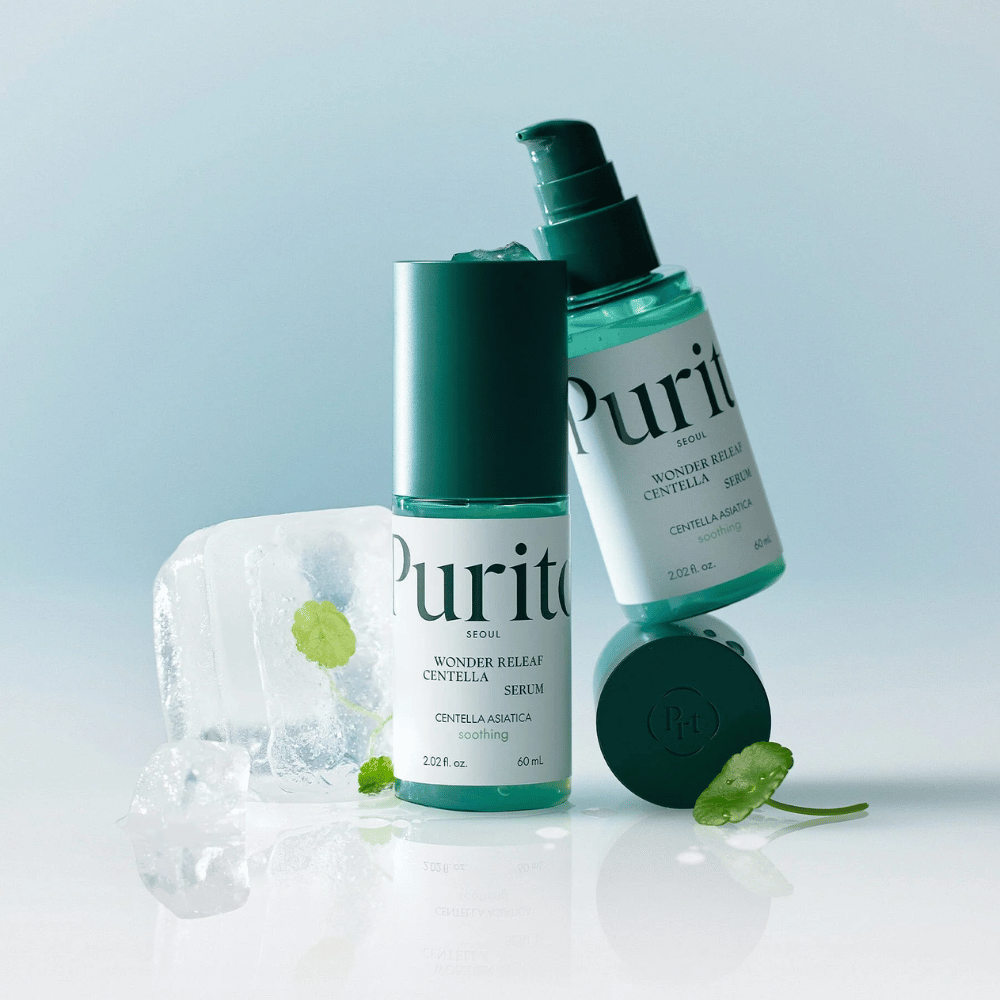 Zwei Flaschen von Purito Wonder Releaf Centella Serum, eine stehend und eine liegend, umgeben von Eiswürfeln mit Centella-Blättern darin sowie ein loses Blatt auf einer hellblauen Fläche.