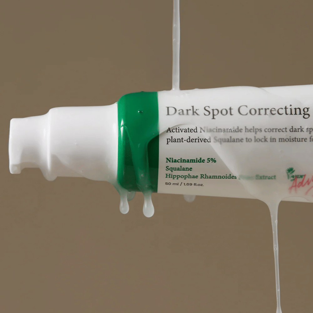 Nahaufnahme einer Pumpflasche von Axis-Y Dark Spot Correcting Glow Serum mit weißer Verpackung und grünem Verschluss, bedeckt von fließender transparenter Flüssigkeit.