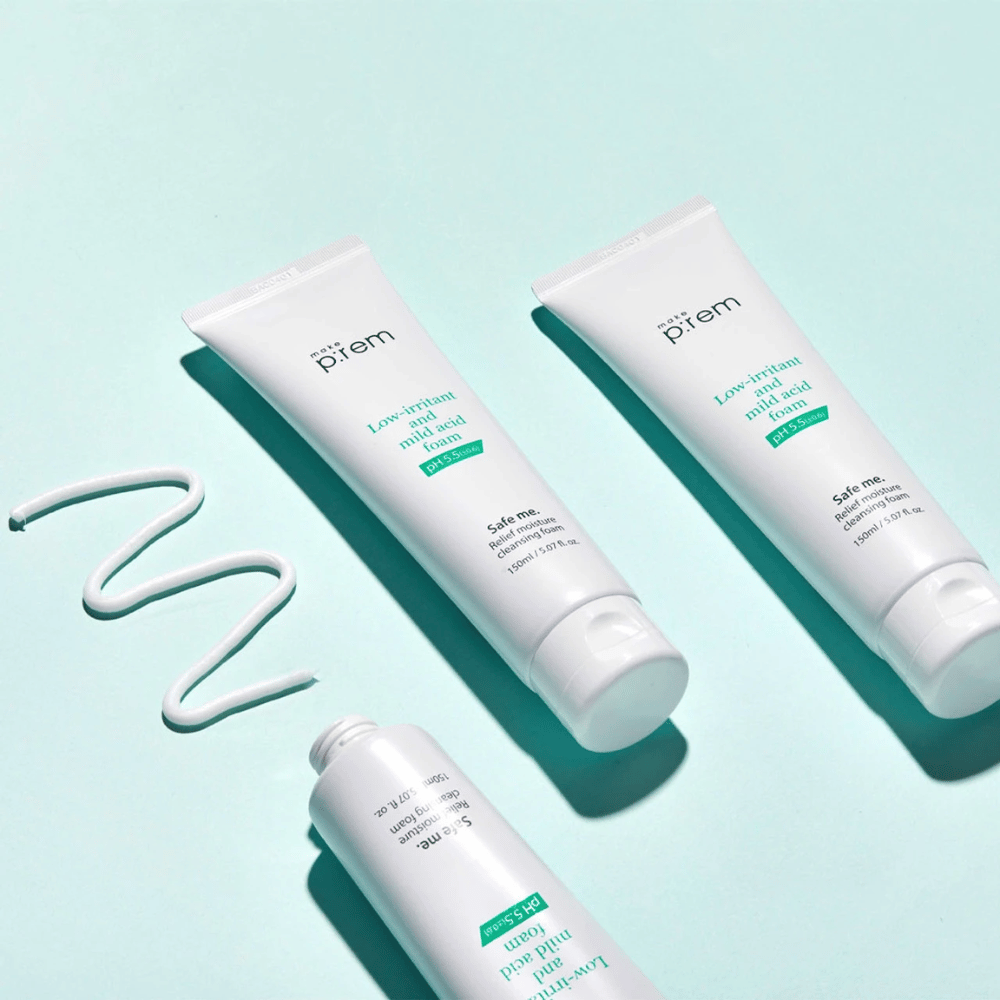 Tre tuber av Make P:rem Safe Me Relief Moisture Cleansing Foam tillsammans med krämiga utklämmade linjer, på en ljus turkos bakgrund.