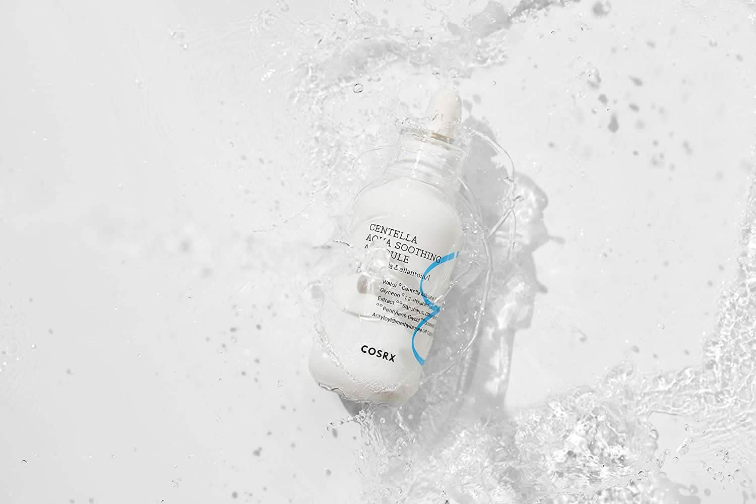 Eine Flasche COSRX Centella Aqua Soothing Ampoule 40ml, die auf eine weiße Fläche spritzt, reduziert Rötungen und bietet beruhigende Feuchtigkeit.