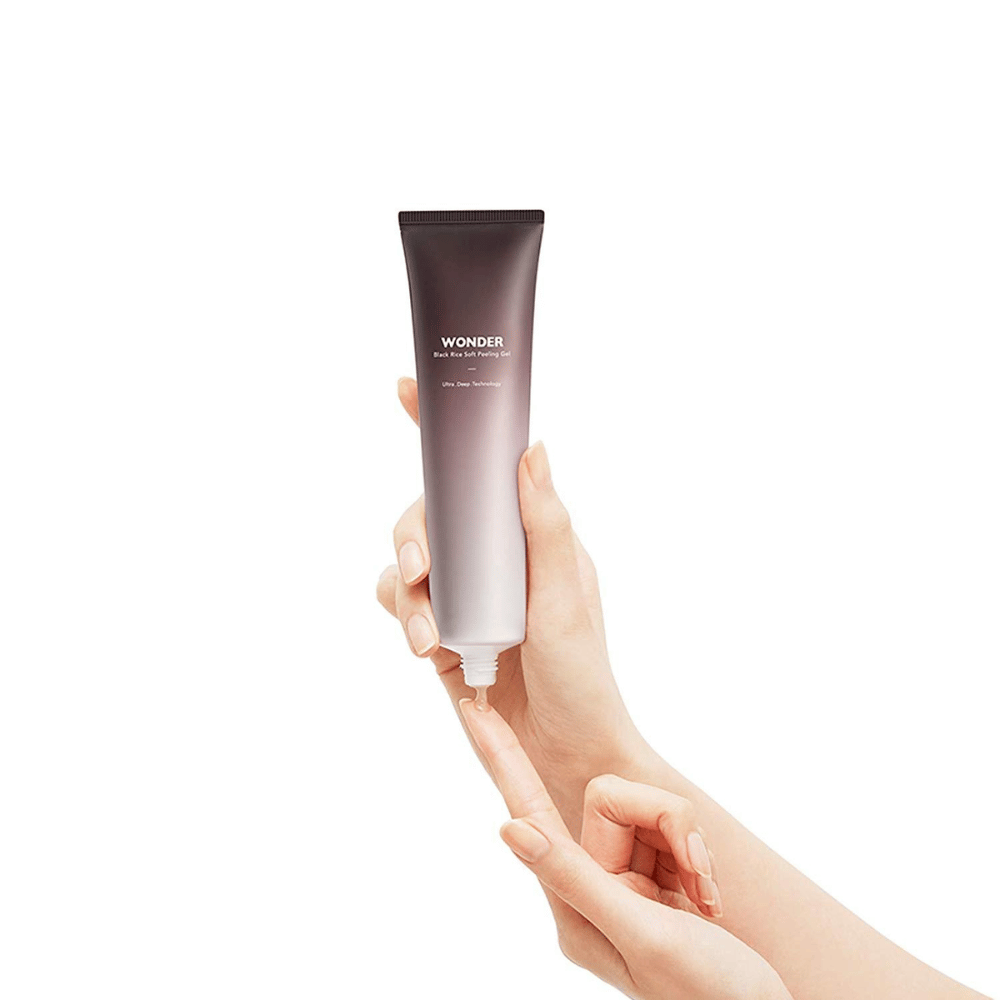 Eine Frauenhand, die eine Tube Haruhuru Wonders Black Rice Soft Peeling Gel 100 ml auf einem weißen Hintergrund hält.