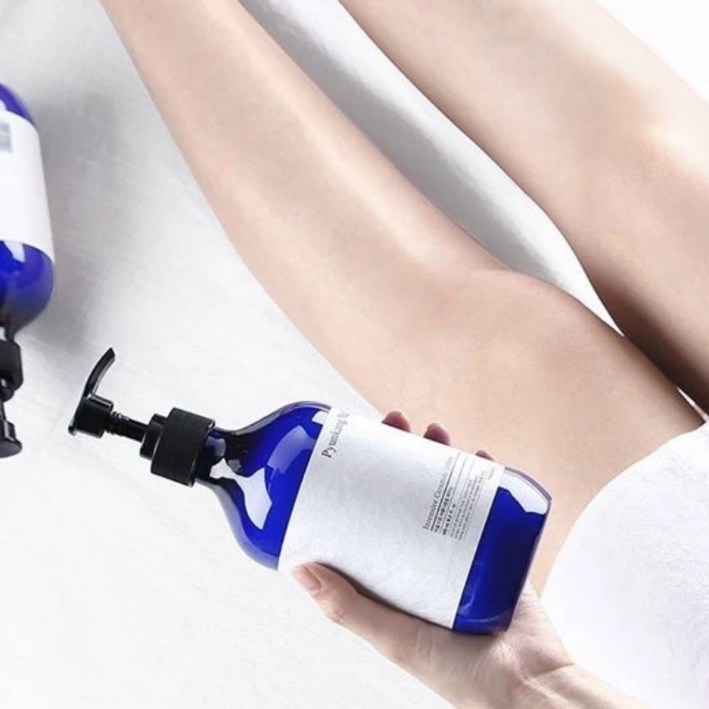 Eine Frau, die eine Flasche Pyunkang Yul Intensive Ceramide Lotion 500ml neben ihren Beinen hält.